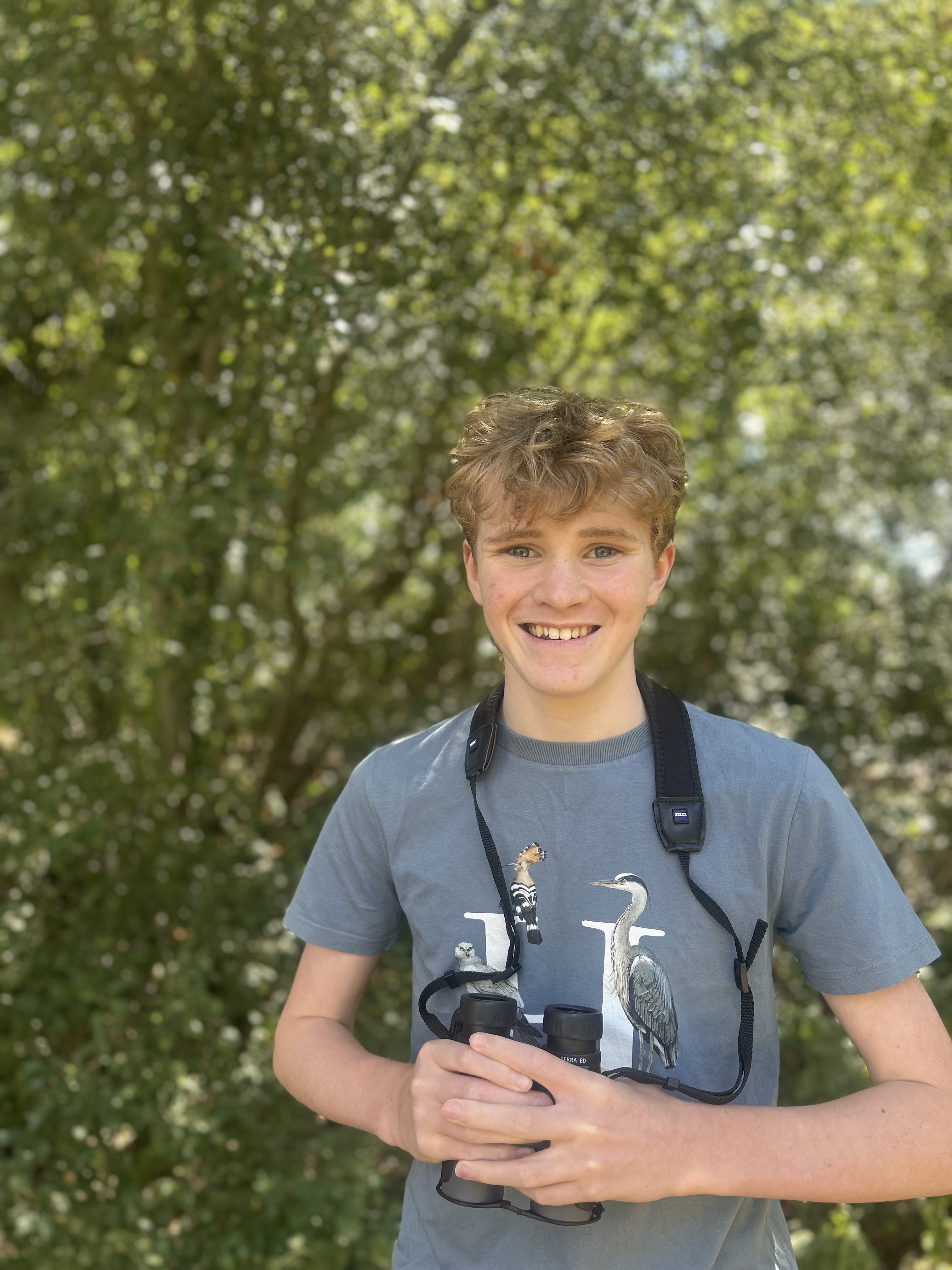 Henry smiling outdoors holding binoculars