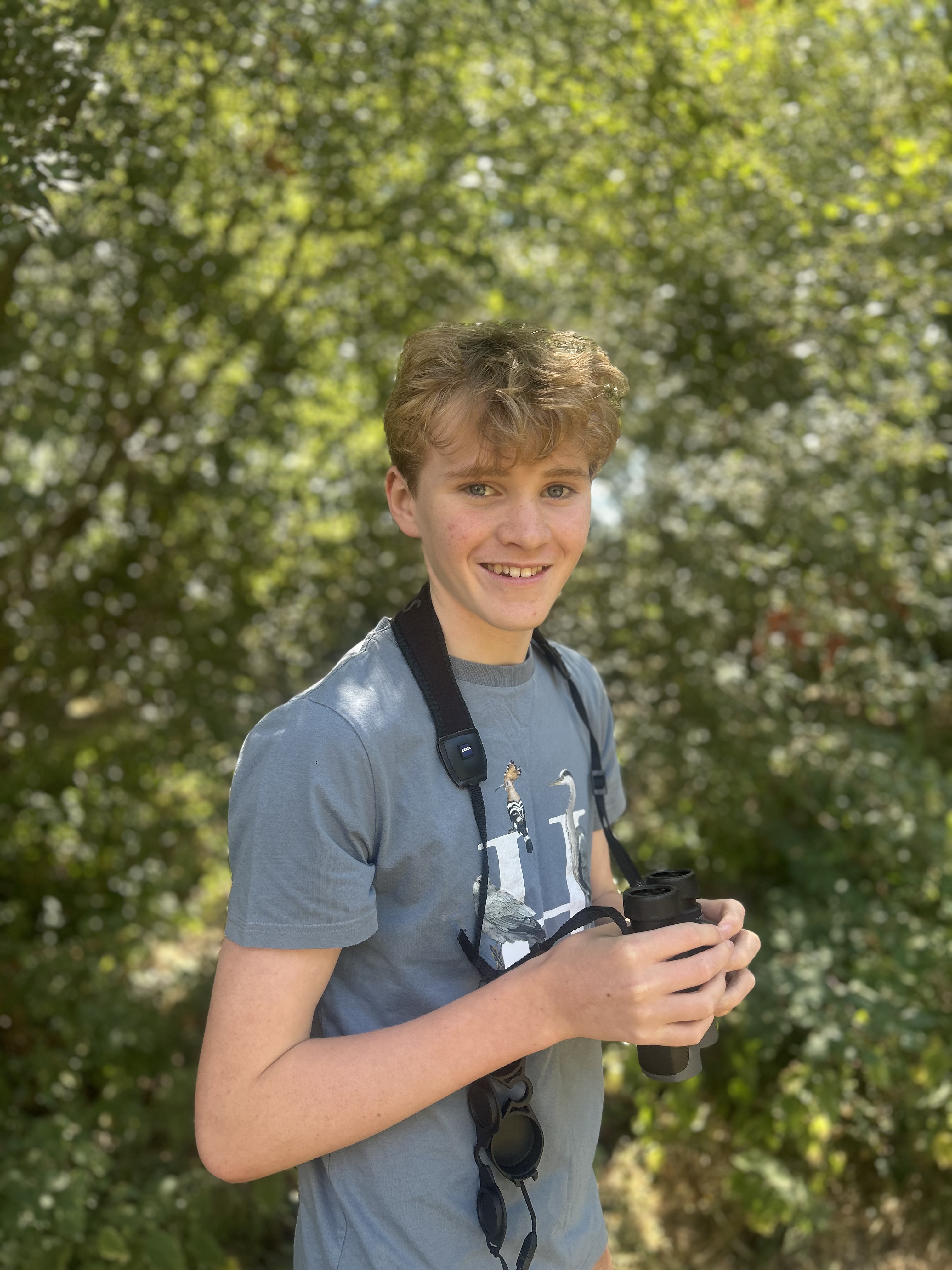 Young birder smiling outdoors holding binoculars
